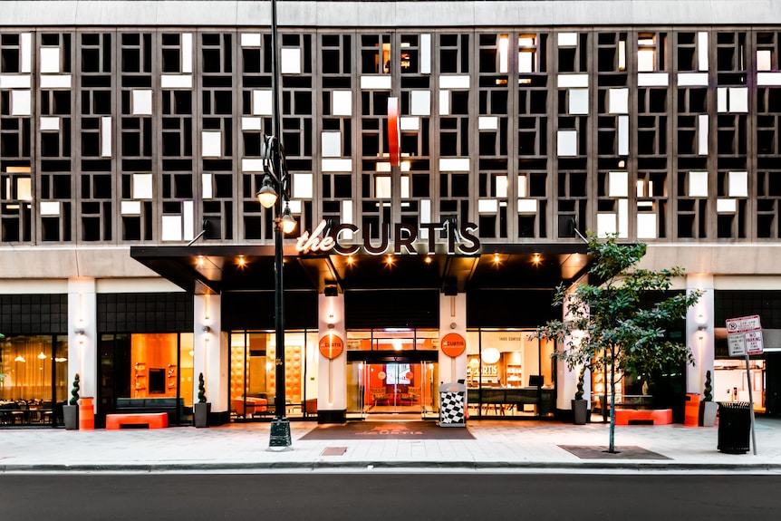 The Curtis hotel entrance on Curtis Street in downtown Denver, lit up at dusk.